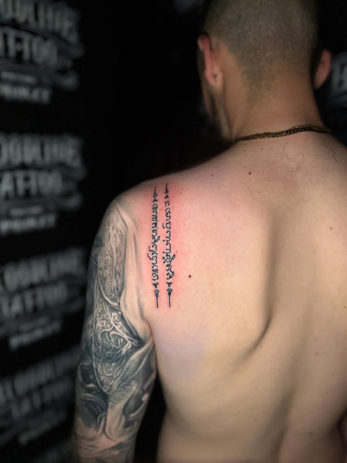 Sak Yant with two parallel vertical columns of Khom script topped with unalome symbols on the left shoulder blade at Bloodline Tattoo Phuket.
