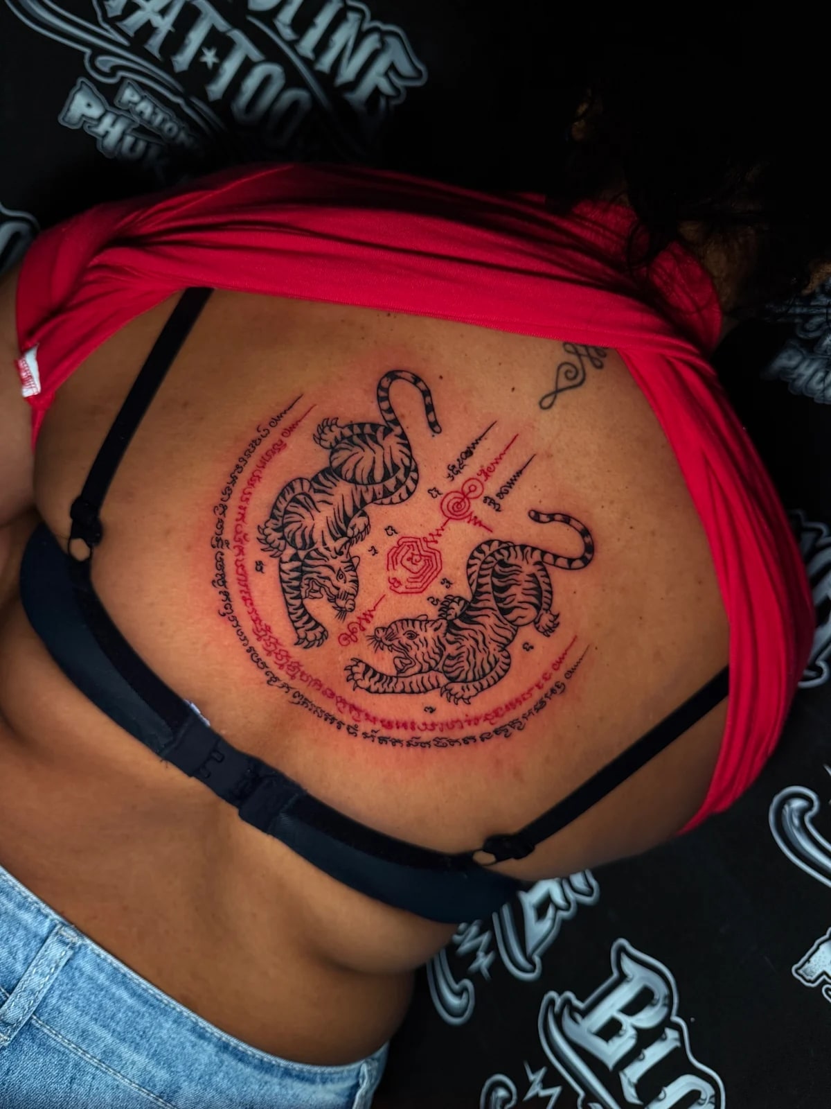 Suea Koo (Twin Tigers) Sak Yant with black-ink tigers and red Khom script in a circular yantra on the upper back at Bloodline Tattoo Phuket.