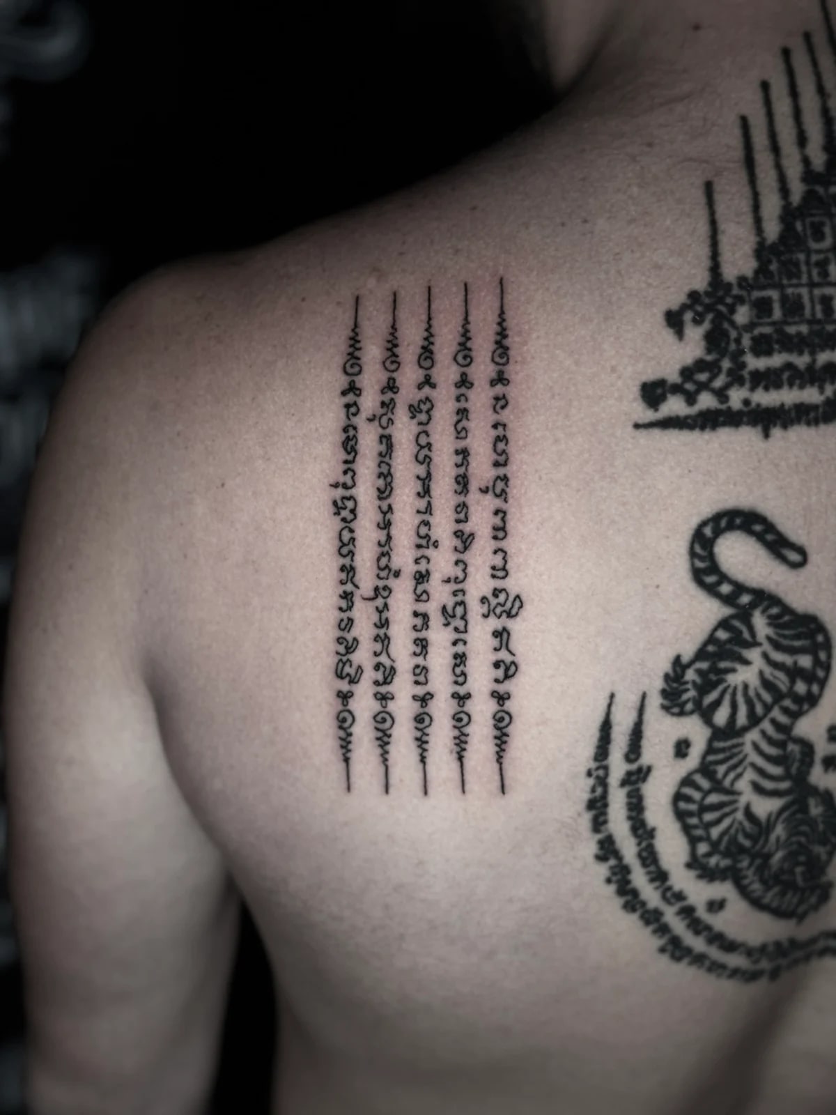 Hah Taew (Five Lines) Sak Yant with five Khom script columns and unalome flourishes on the left shoulder blade at Bloodline Tattoo Phuket.
