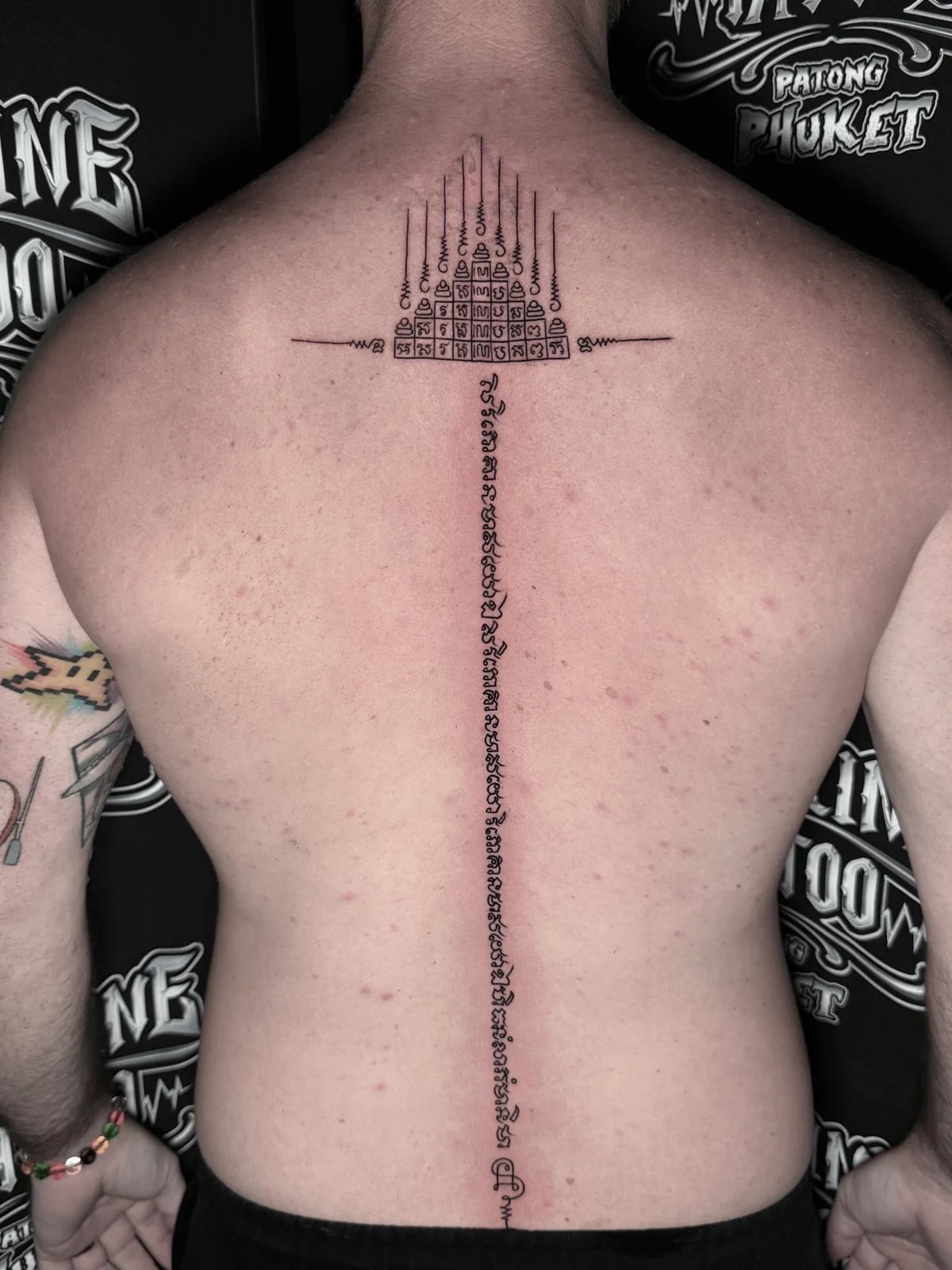 Gao Yord (Nine Spires) Sak Yant with a geometric yantra grid and a long vertical Khom script column down the spine at Bloodline Tattoo Phuket.
