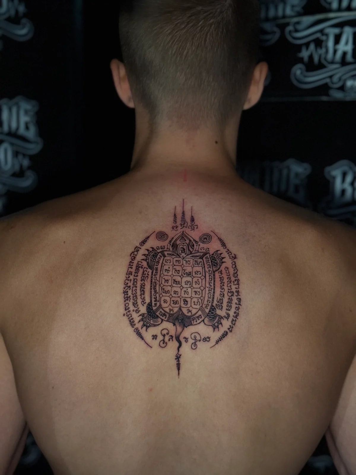 Yant Tao Ruean (Turtle) Sak Yant with a script-filled shell grid, circular Khom borders, and unalome spires on the upper back at Bloodline Tattoo Phuket.
