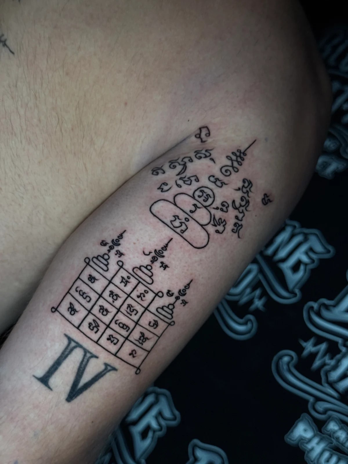 Sak Yant talismanic grid yantra with sixteen Khom script cells, tiered script design, unalomes, and Roman numeral IV on the inner arm at Bloodline Tattoo Phuket.