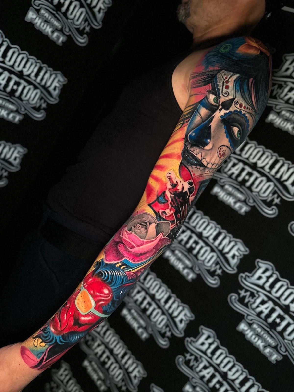 Colour sleeve with a Santa Muerte portrait, a pink rose, and a red demonic face on yellow and blue ornamental backgrounds at Bloodline Tattoo Phuket.