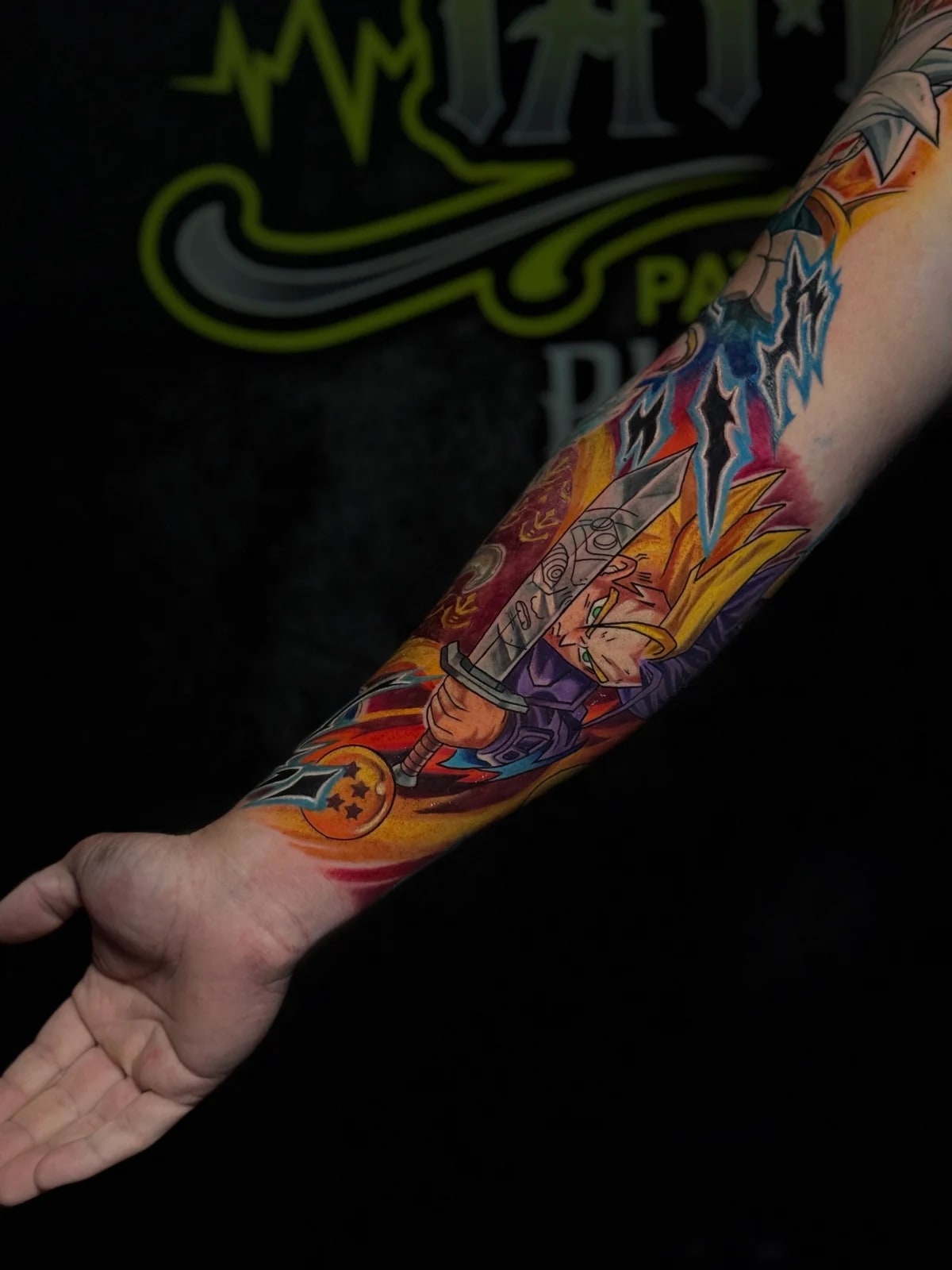 Colour forearm tattoo of Super Saiyan Trunks wielding his sword beside a four-star Dragon Ball with blue energy effects at Bloodline Tattoo Phuket.