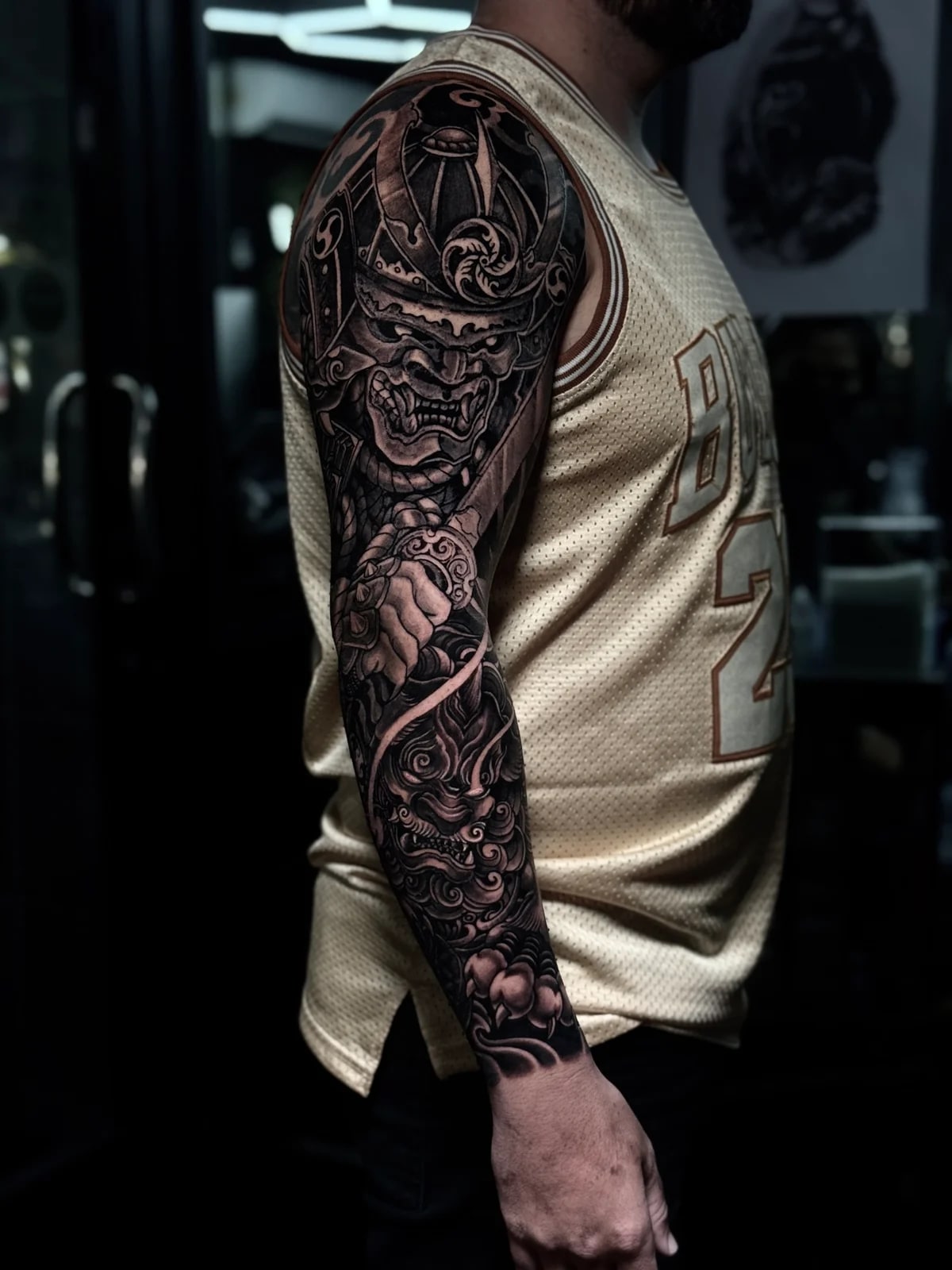 Japanese black and grey full sleeve with fierce samurai menpo gripping a katana and Komainu lion-dog on the forearm amid clouds at Bloodline Tattoo Phuket.