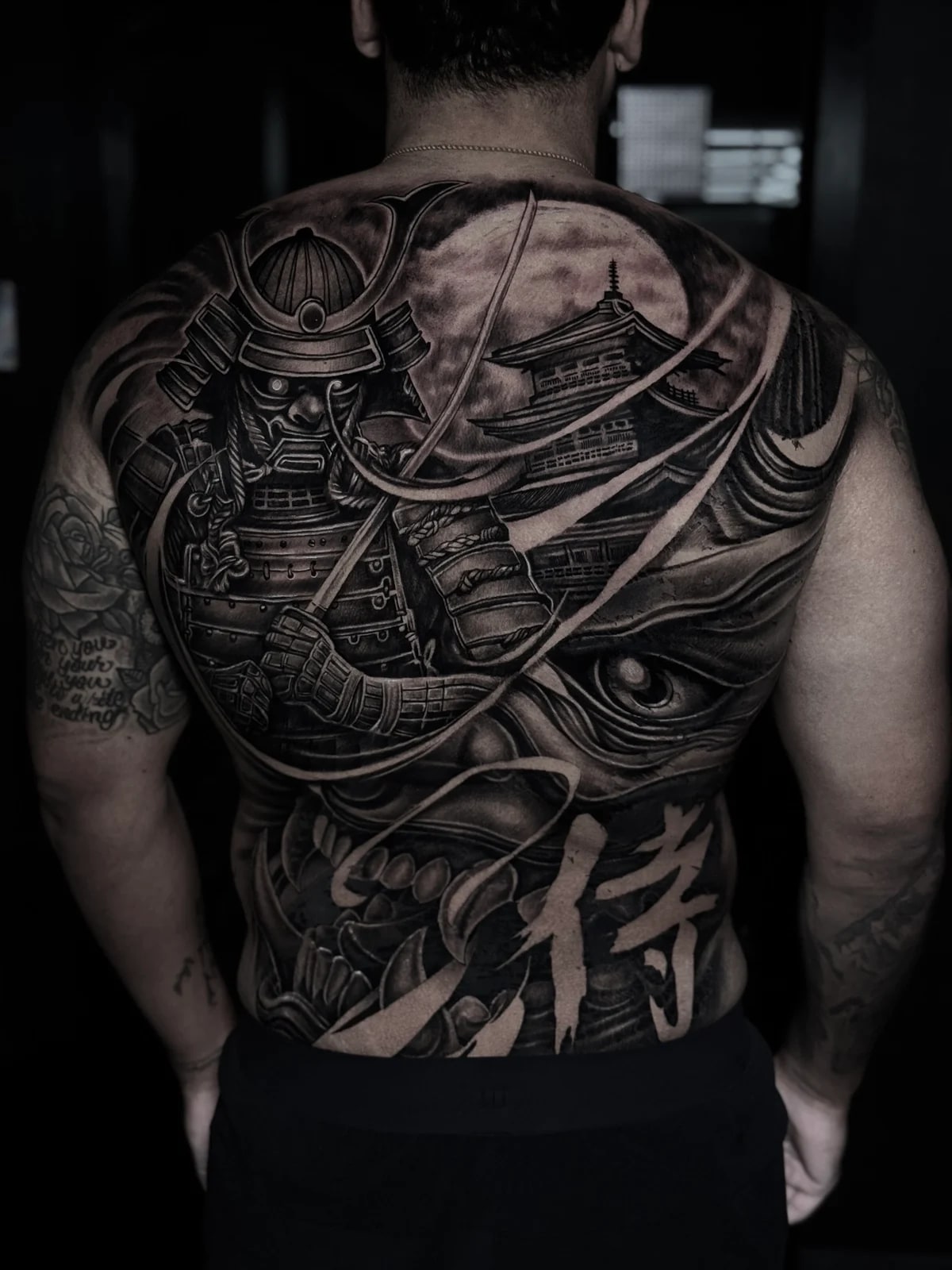 Japanese black and grey full-back piece with armored samurai, pagoda under a full moon, Hannya mask, and kanji at Bloodline Tattoo Phuket.