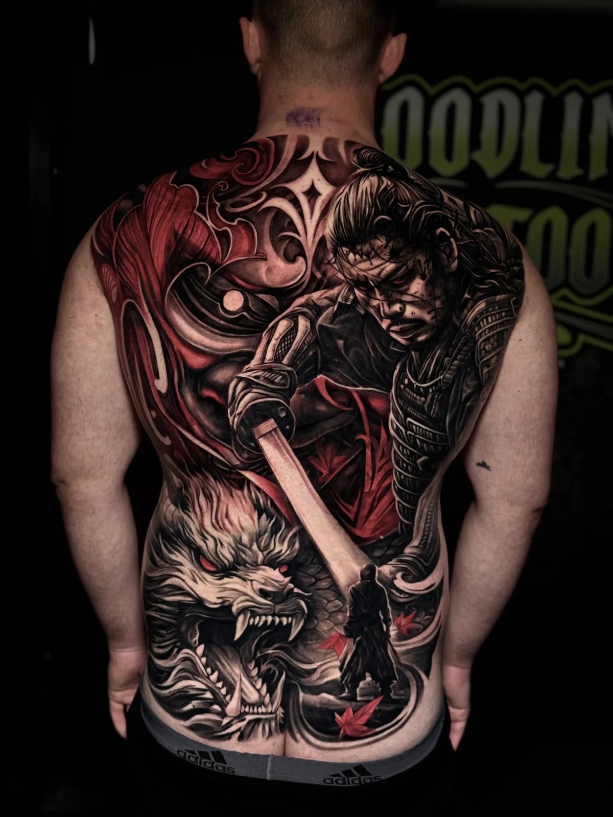 Japanese full-back tattoo with fierce samurai, glowing katana, snarling dragon with red eyes, and red maple leaves at Bloodline Tattoo Phuket.