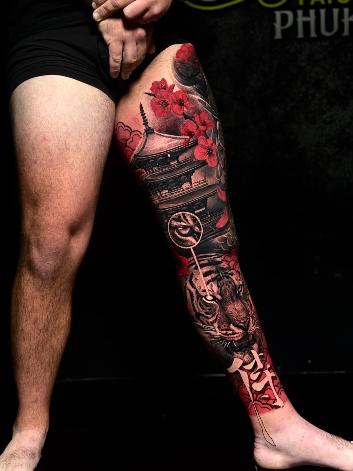 Japanese full leg sleeve with pagoda, red cherry blossoms, tiger head on the shin, and bold kanji at the ankle at Bloodline Tattoo Phuket.