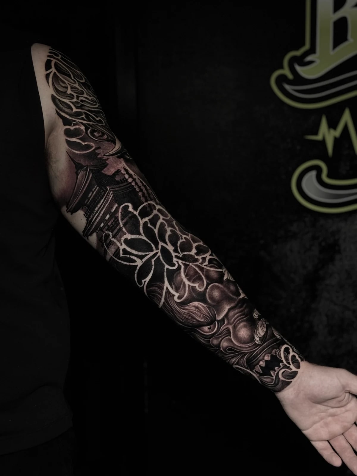 Japanese black and grey full sleeve with pagoda in the clouds, bold chrysanthemum, and fierce foo dog on the forearm at Bloodline Tattoo Phuket.