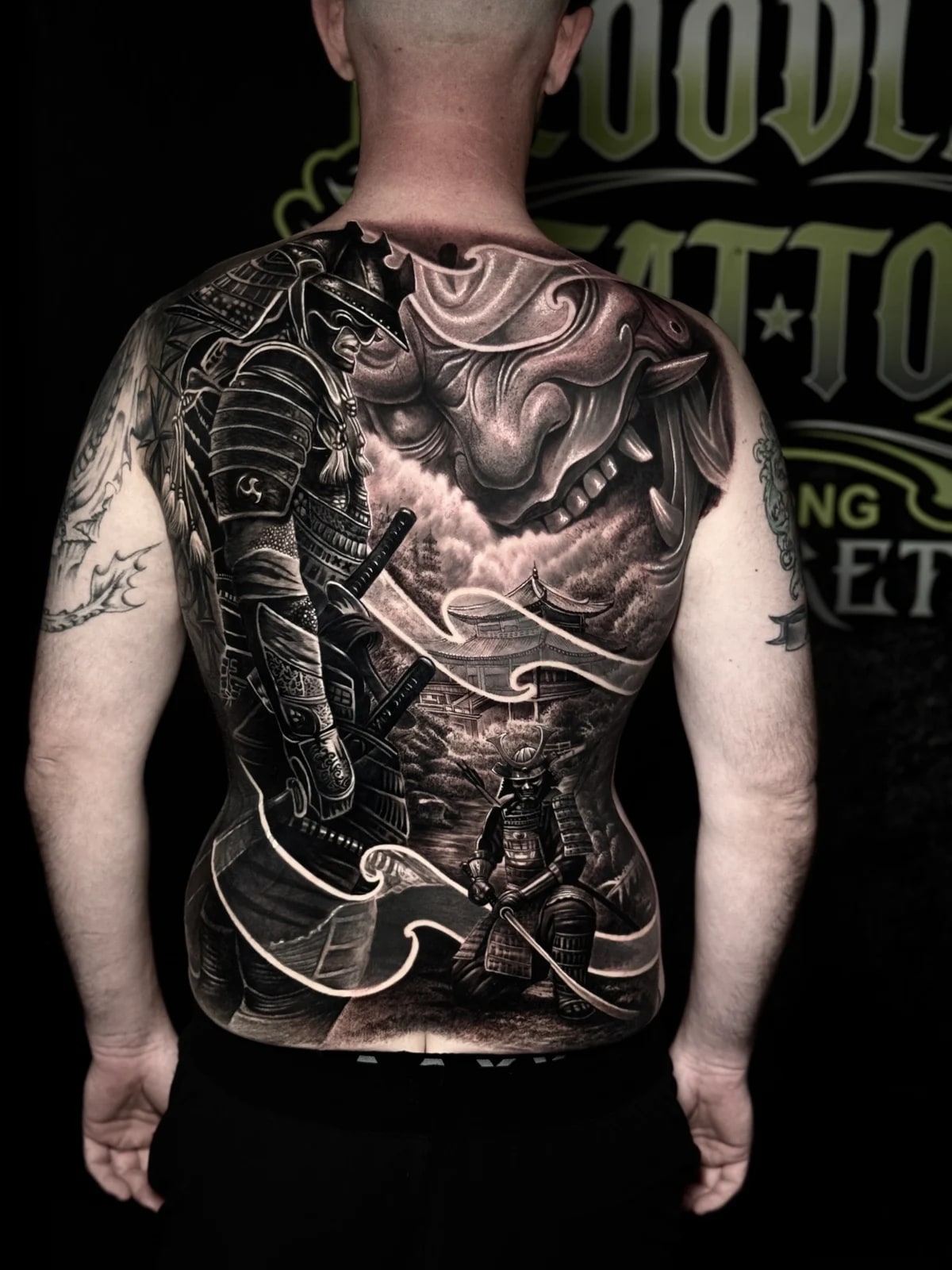 Japanese black and grey full-back with armored samurai, Hannya mask, pagoda in mist, kneeling swordsman, and flowing wind lines at Bloodline Tattoo Phuket.
