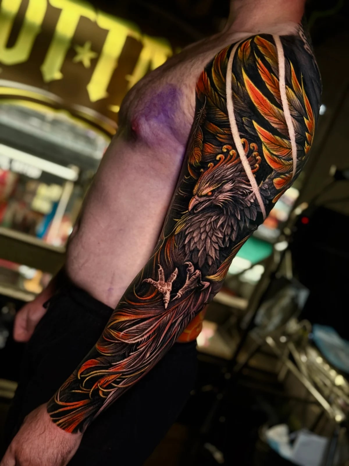 Japanese full sleeve with fierce phoenix in orange and yellow feathers, glowing red eye, and bold white negative-space bands at Bloodline Tattoo Phuket.