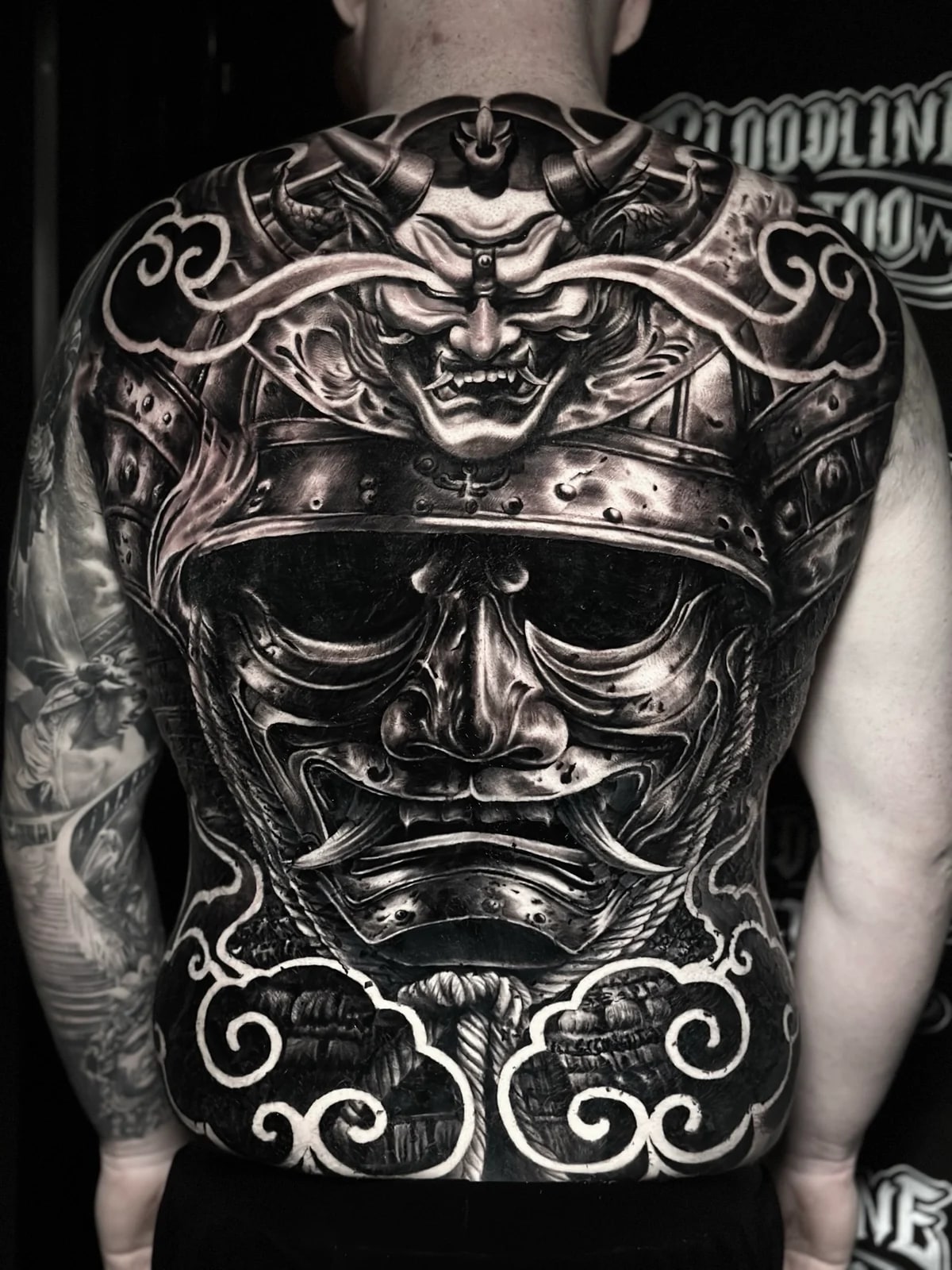 Japanese black and grey full-back samurai menpo and kabuto with horned Hannya crest framed by high-contrast stylized clouds at Bloodline Tattoo Phuket.