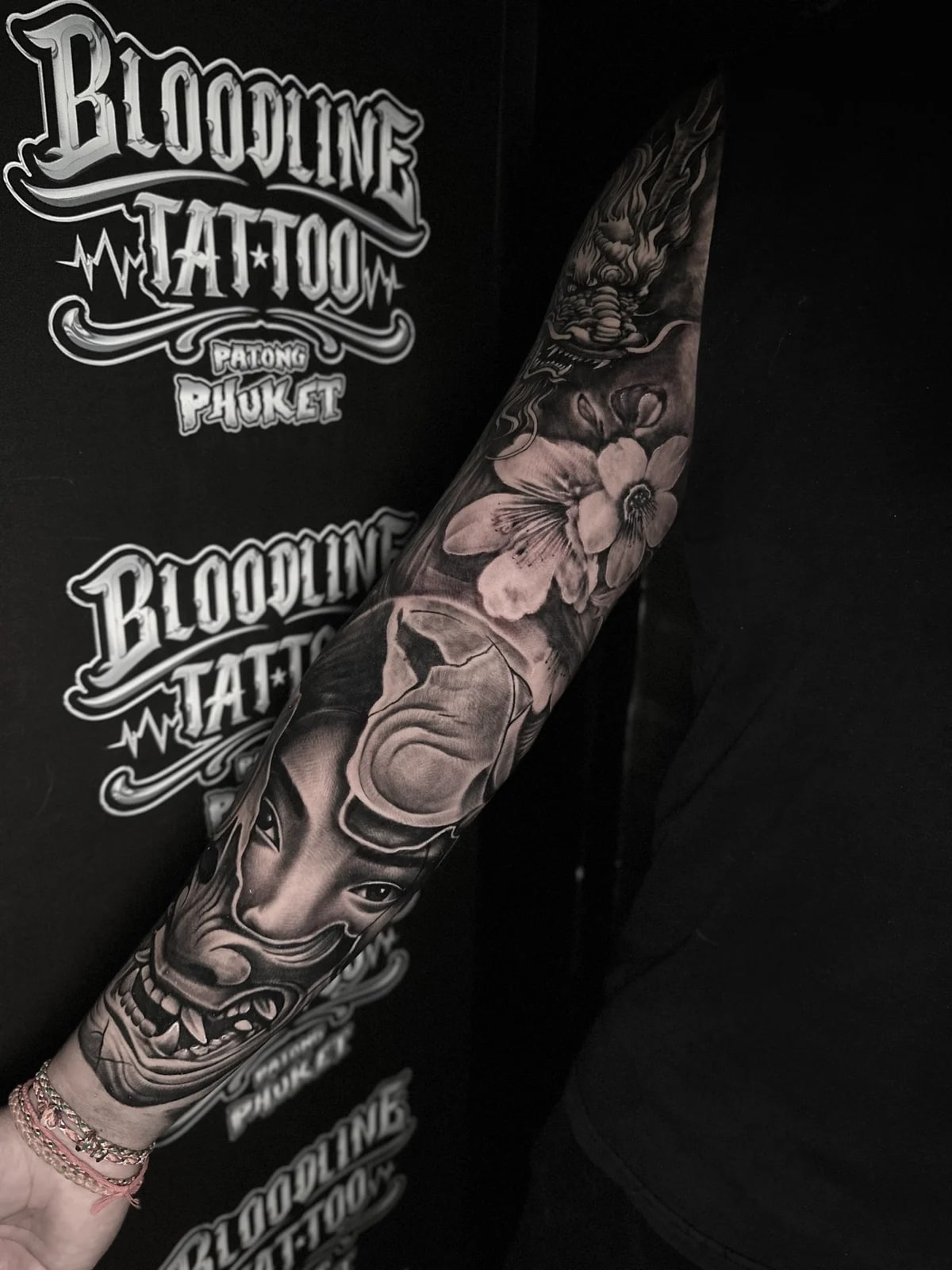 Japanese black and grey full sleeve with Hannya mask, woman's portrait, floral blooms, and dragon head at Bloodline Tattoo Phuket.
