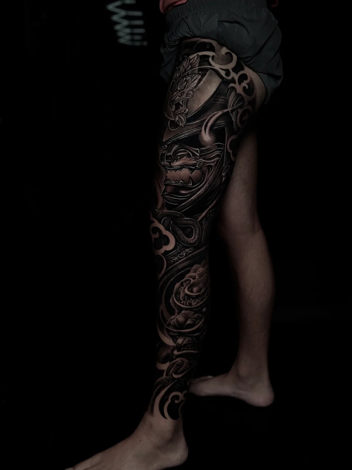 Japanese black and grey full leg sleeve with kabuto and mempo on the thigh and foo dog amid swirling clouds and water to the ankle at Bloodline Tattoo Phuket.