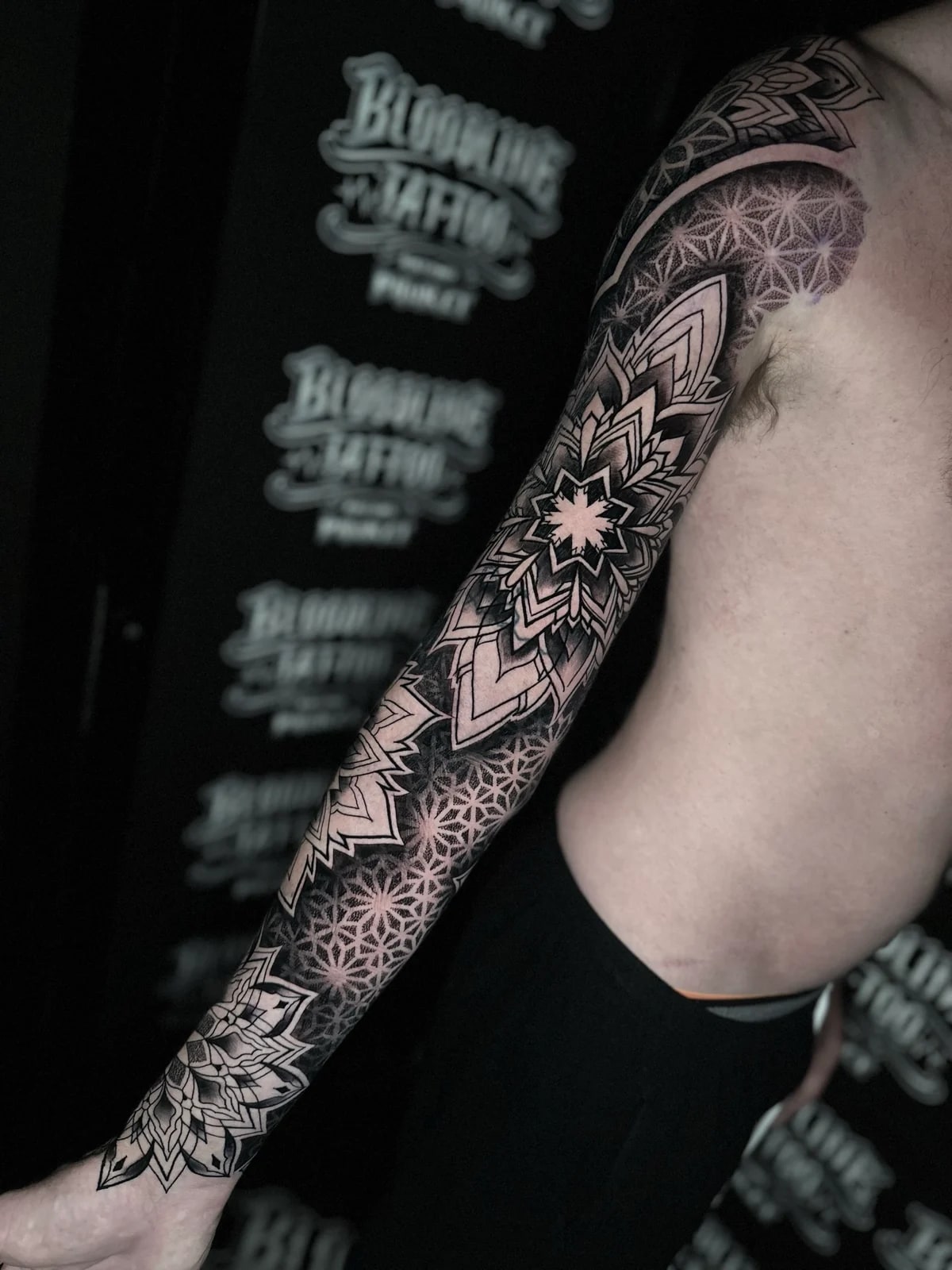 Geometric mandala dotwork full sleeve with large elbow and wrist mandalas set in a repeating sacred-geometry star grid at Bloodline Tattoo Phuket.