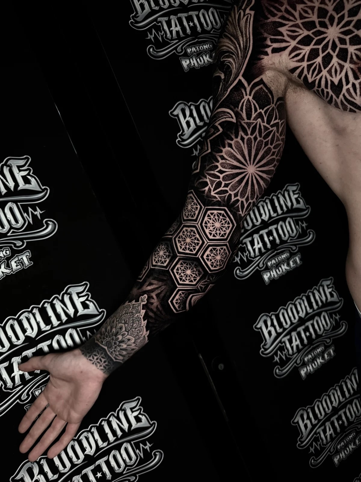 Chest mandala and full arm sleeve with dotwork lotus patterns, overlapping shoulder mandalas, and hexagonal forearm geometry at Bloodline Tattoo Phuket.
