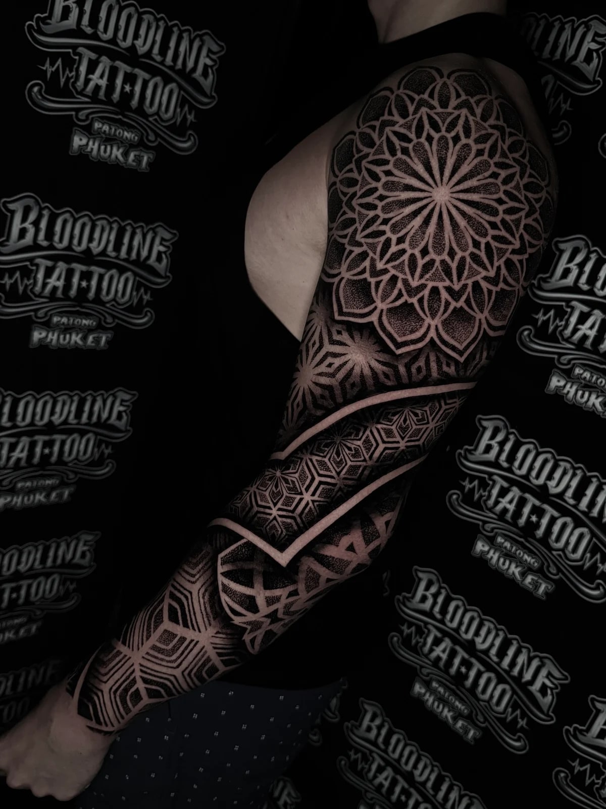 Mandala dotwork sleeve with a large shoulder lotus, diagonal negative-space bands, and a dense hexagonal forearm pattern at Bloodline Tattoo Phuket.