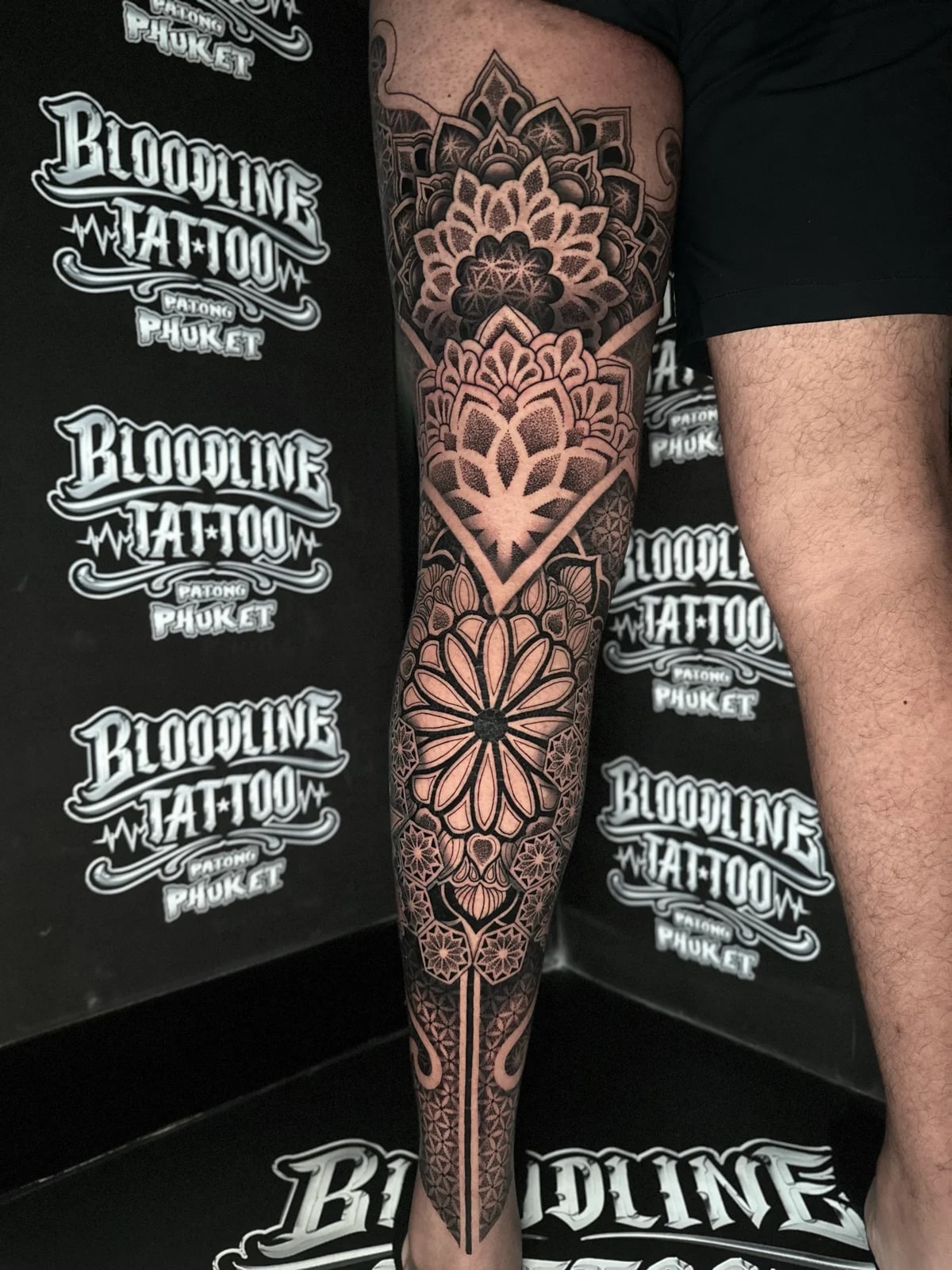 Stacked blackwork leg mandalas with a thigh lotus, a diamond-framed knee floral, and a circular shin mandala with ankle geometry at Bloodline Tattoo Phuket.