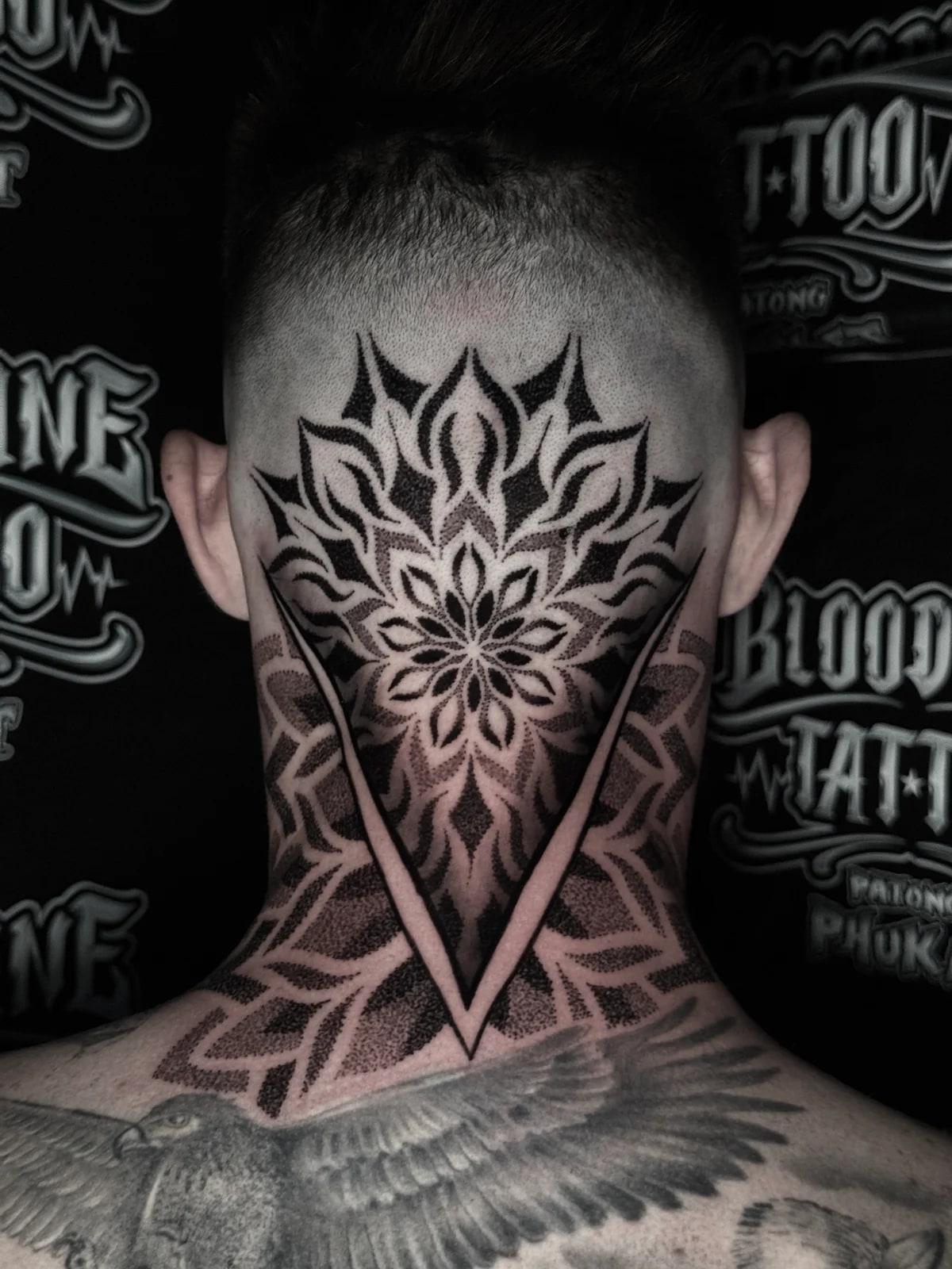 Back-of-head occipital lotus mandala flowing into a triangular neck geometric panel with stippled dotwork at Bloodline Tattoo Phuket.