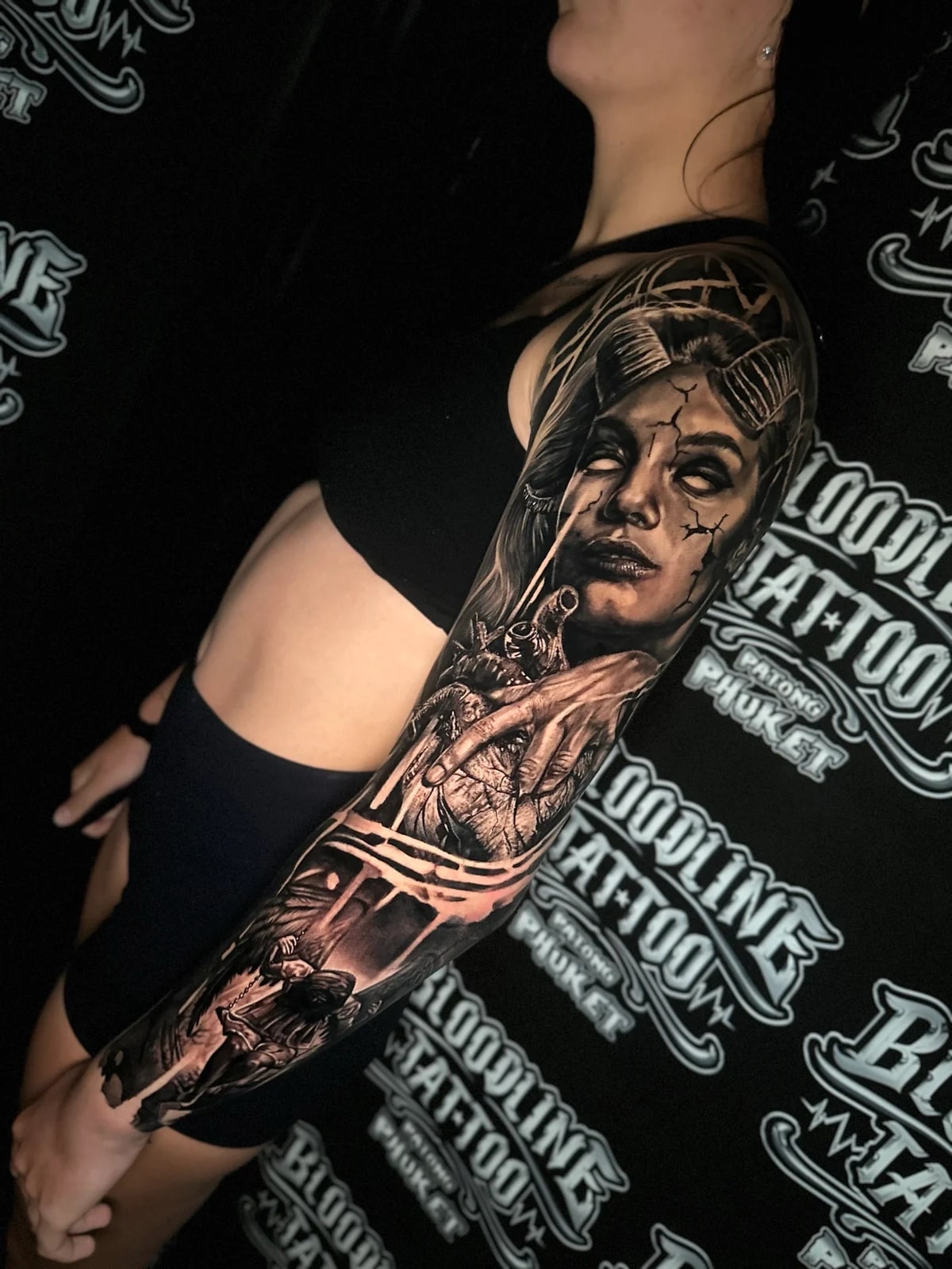 Detailed black and grey realism full sleeve tattoo featuring a horned demon woman with white eyes, anatomical heart, and hooded winged reaper at Bloodline Tattoo Phuket.