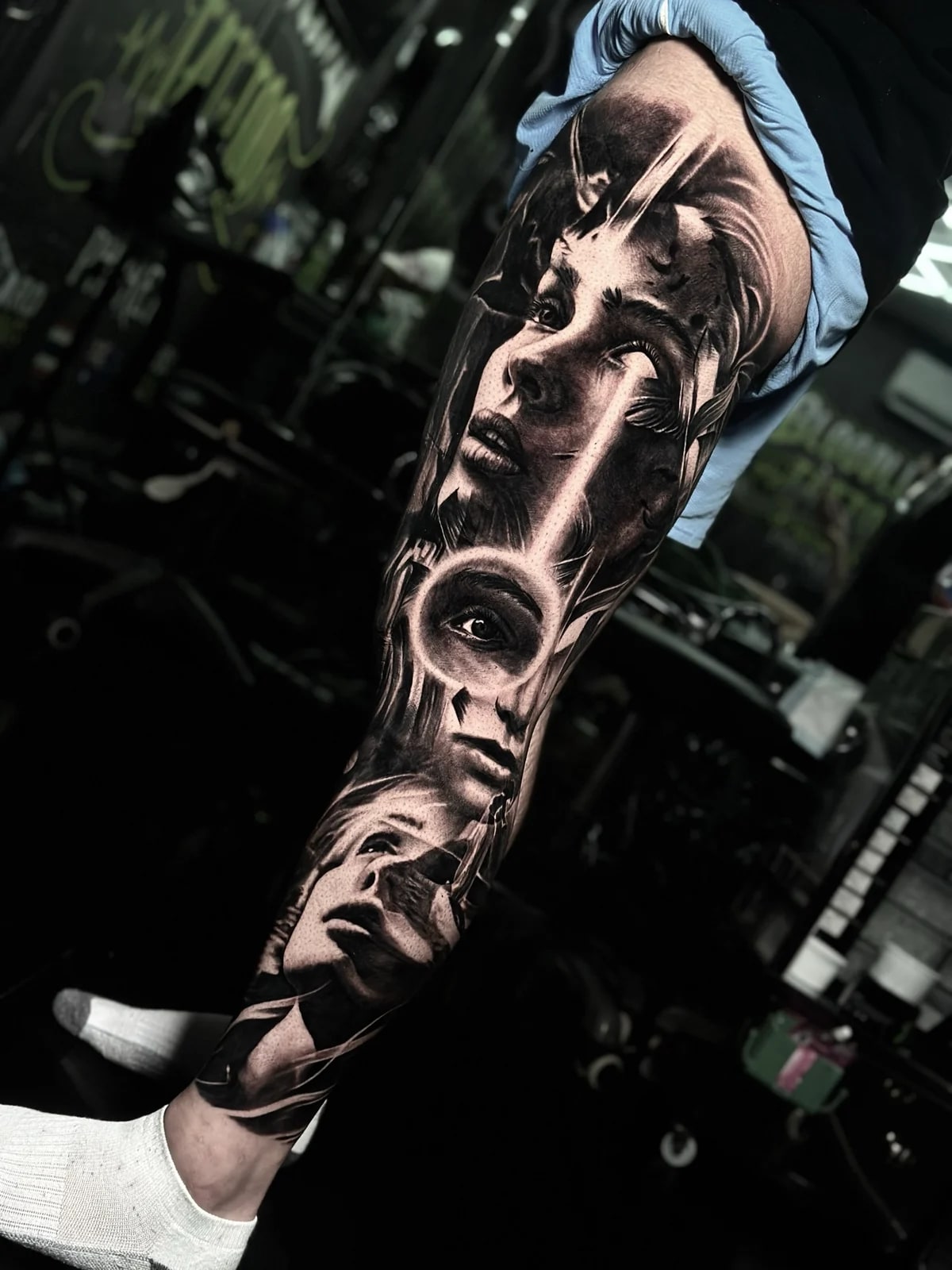 Detailed black and grey realism full leg sleeve tattoo featuring multiple realistic women's portraits with glowing halos and dramatic light rays at Bloodline Tattoo Phuket.