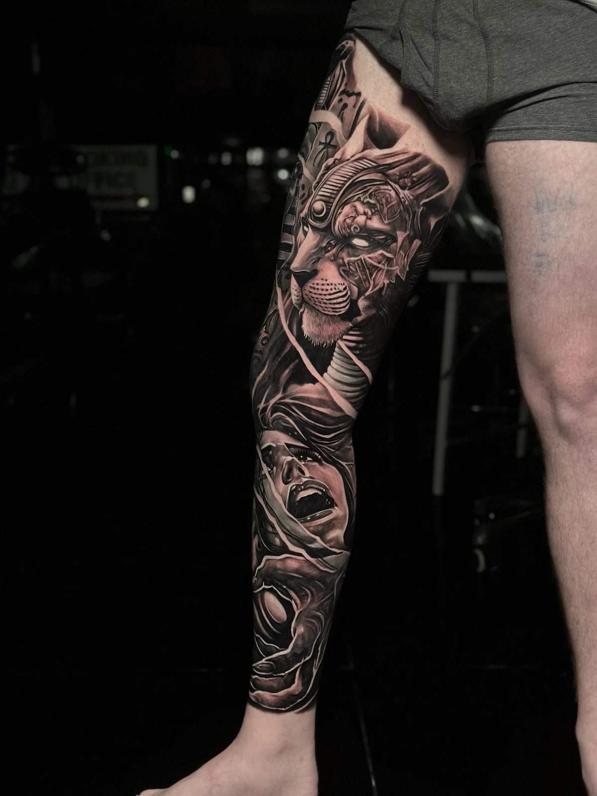 Detailed black and grey realism full leg sleeve tattoo featuring a biomechanical lion with glowing eyes, screaming woman, and reaching hand at Bloodline Tattoo Phuket.