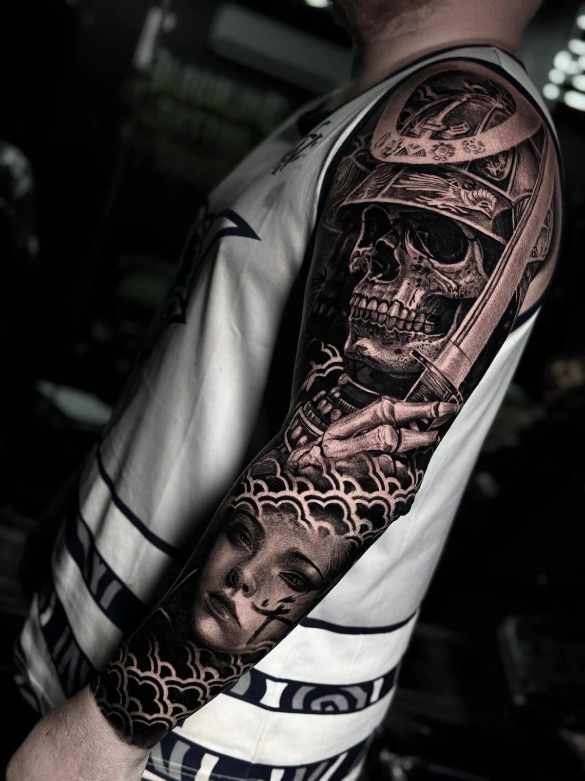 Detailed black and grey realism full sleeve tattoo featuring a samurai skull in a kabuto helmet with katana, woman's portrait, and Japanese cloud patterns at Bloodline Tattoo Phuket.