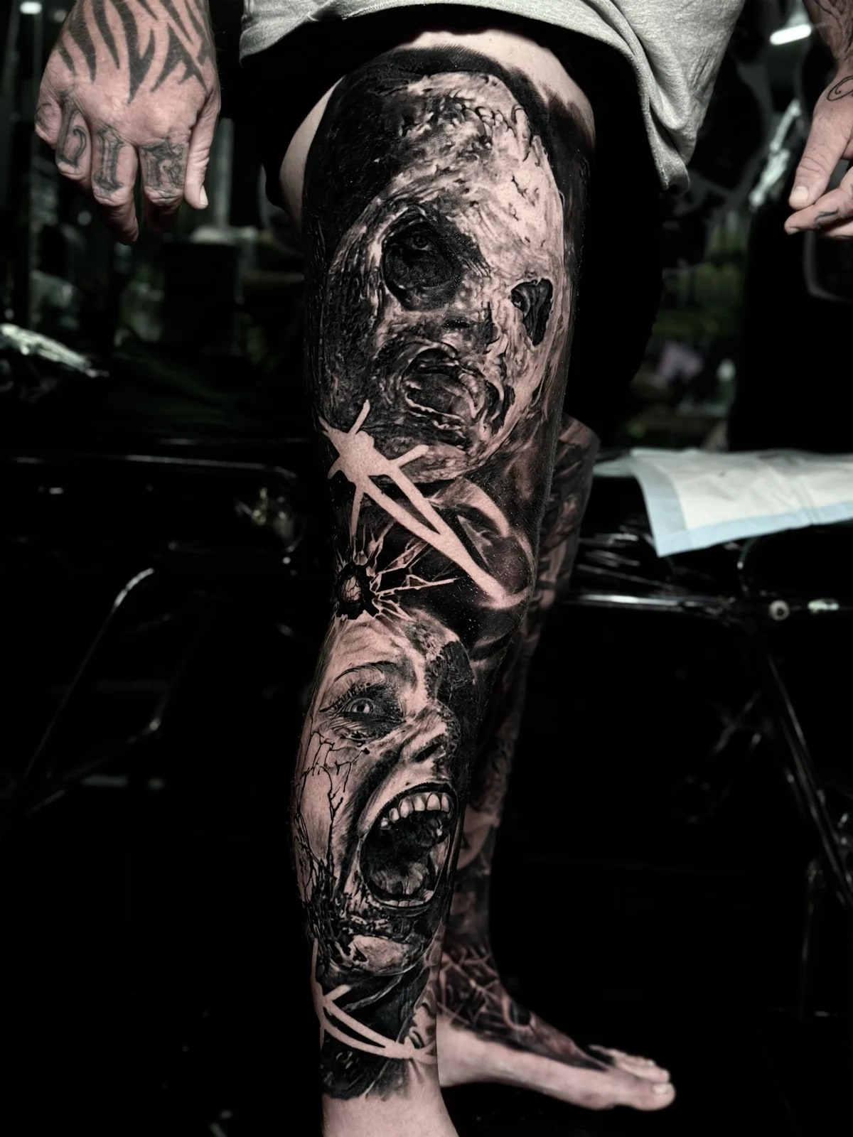 Detailed black and grey realism full leg sleeve tattoo featuring a Leatherface-style stitched mask and a woman screaming in terror at Bloodline Tattoo Phuket.