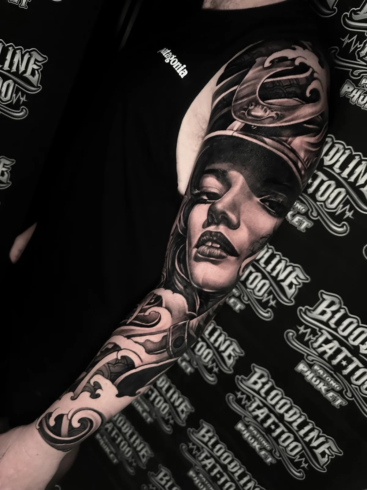 Detailed black and grey realism full sleeve tattoo featuring a realistic woman's portrait with Japanese wave motifs at Bloodline Tattoo Phuket.