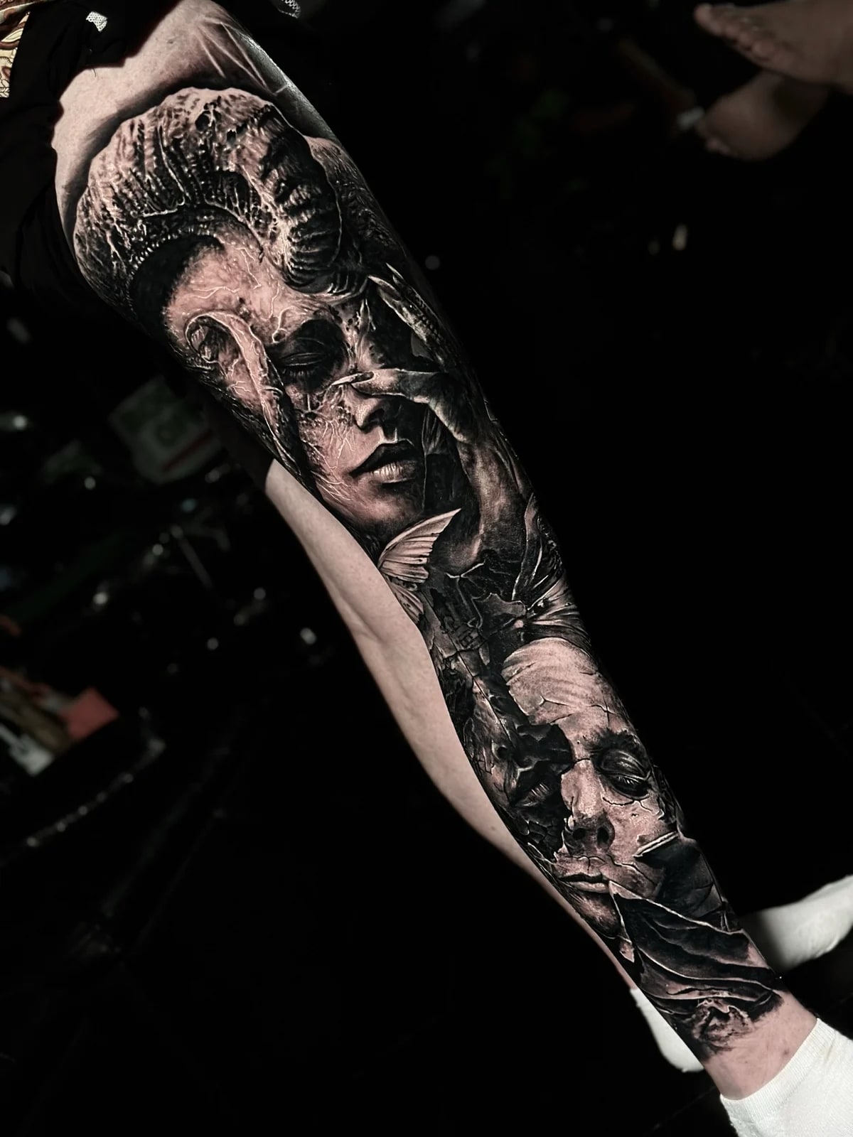 Detailed black and grey realism full leg sleeve tattoo featuring a woman with ram horn, skeletal clawed hand, and cracked Michael Myers mask at Bloodline Tattoo Phuket.