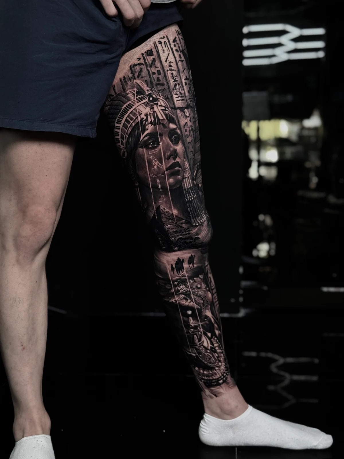 Detailed black and grey realism full leg sleeve tattoo featuring an Egyptian queen with hieroglyphics, pyramid, camel caravan, and pharaoh portrait at Bloodline Tattoo Phuket.