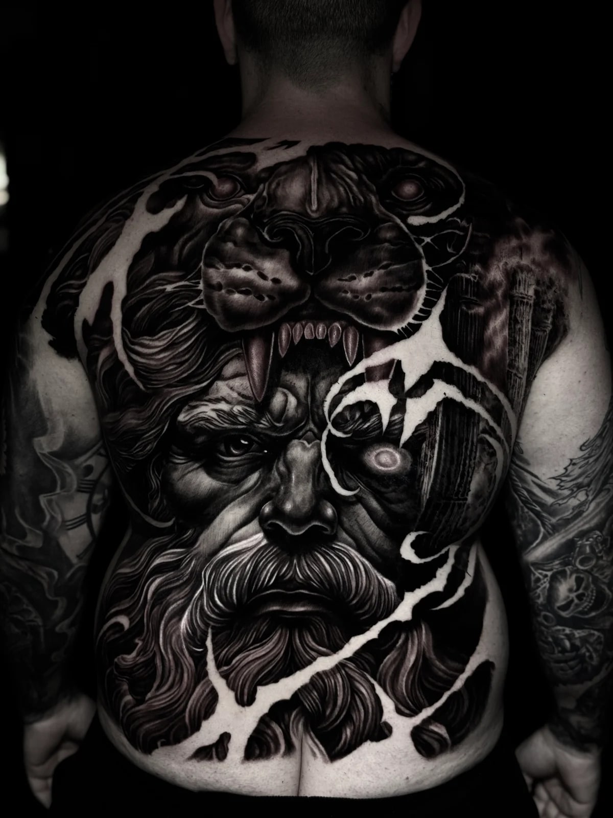 Detailed black and grey realism full back tattoo featuring Hercules in a lion-head cowl with glowing eye, classical columns, and lightning-torn composition at Bloodline Tattoo Phuket.