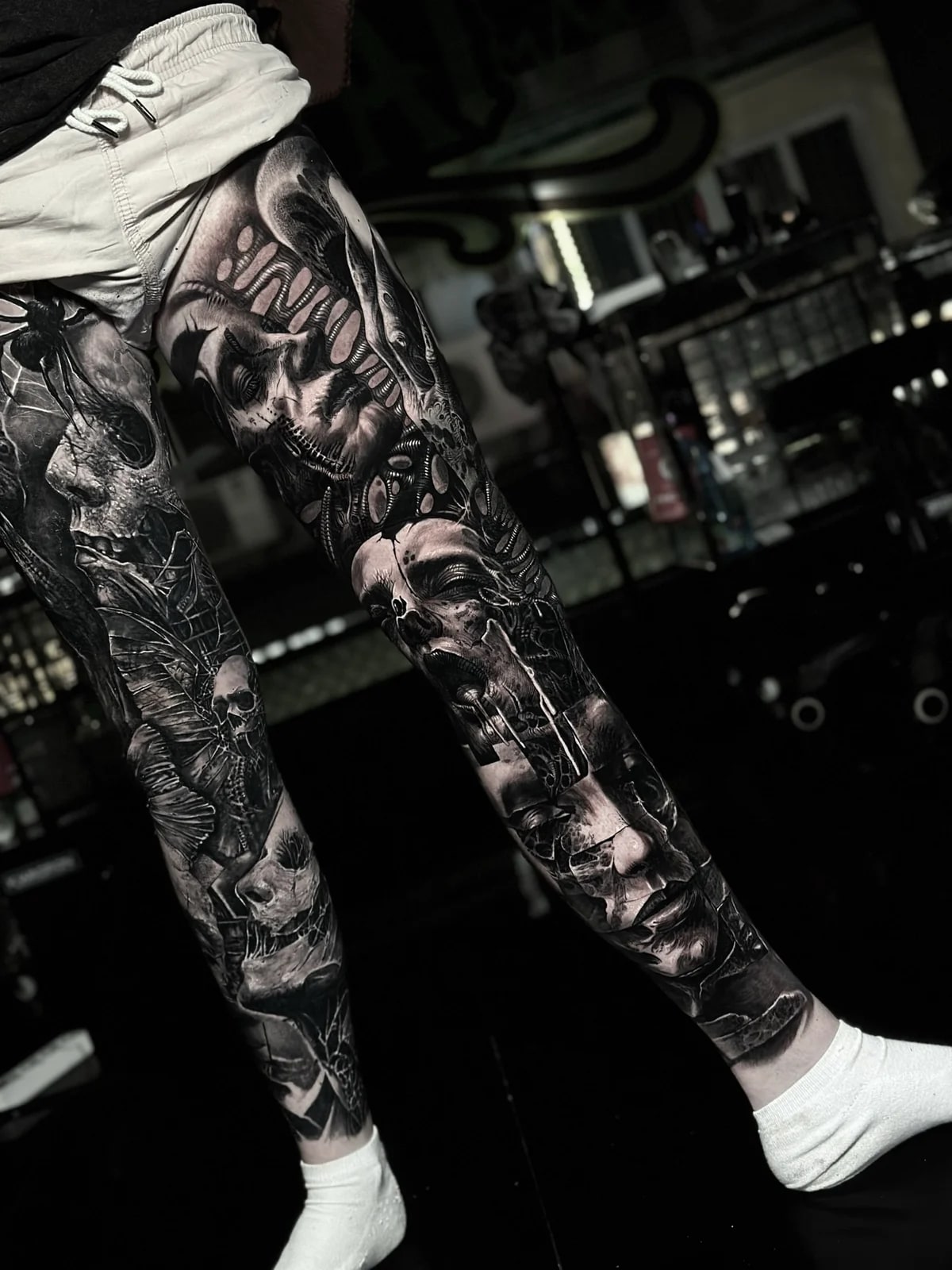 Intricate black and grey realism full leg sleeve tattoo featuring surreal biomechanical human faces with rib-like structures and screaming expressions at Bloodline Tattoo Phuket.