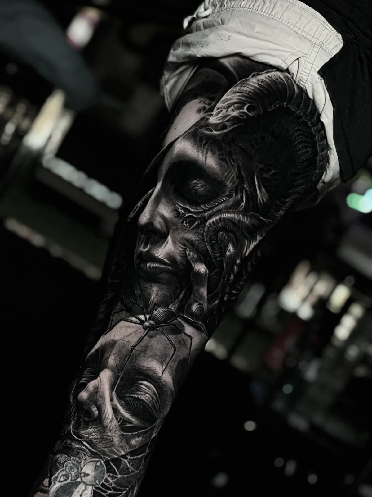 Intricate black and grey realism tattoo featuring a surreal biomechanical woman's face, organic textures, and a large spider over a second face at Bloodline Tattoo Phuket.