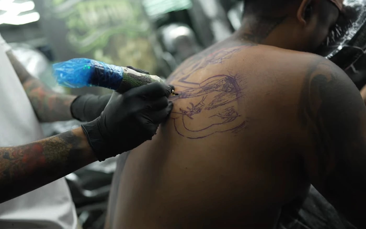 Gloved artist starting a tattoo over a stencil with a barrier-wrapped machine at Bloodline Tattoo Phuket