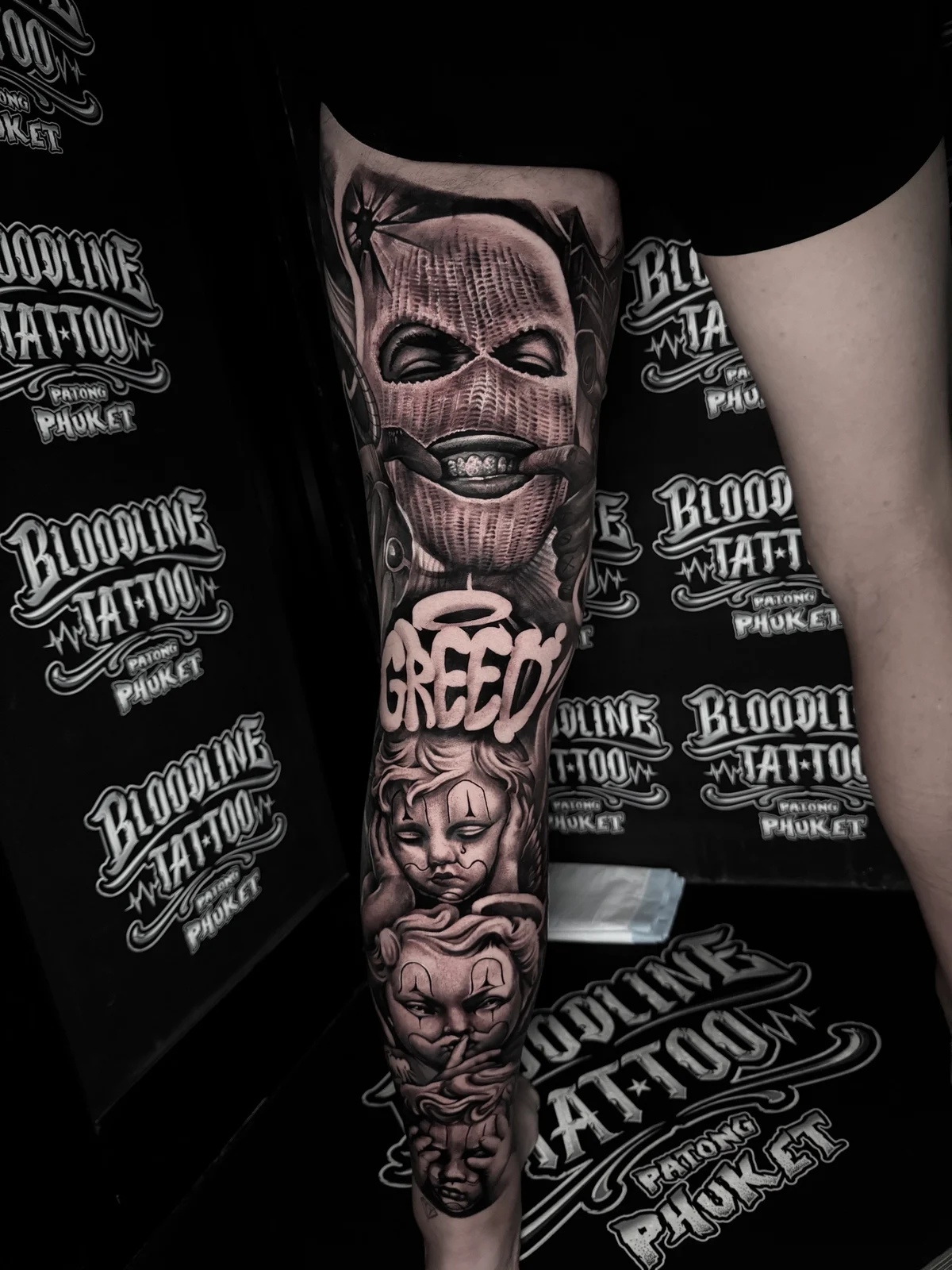 Chicano Greed script leg sleeve with balaclava grill and three wise monkeys payasas at Bloodline Tattoo Phuket.