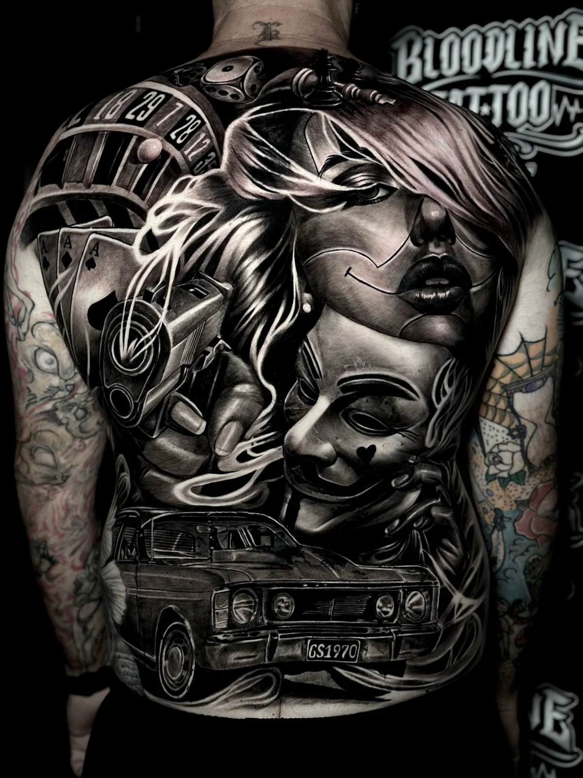 Chicano back tattoo with roulette, payasa portrait, handgun, playing cards, and lowrider at Bloodline Tattoo Phuket.