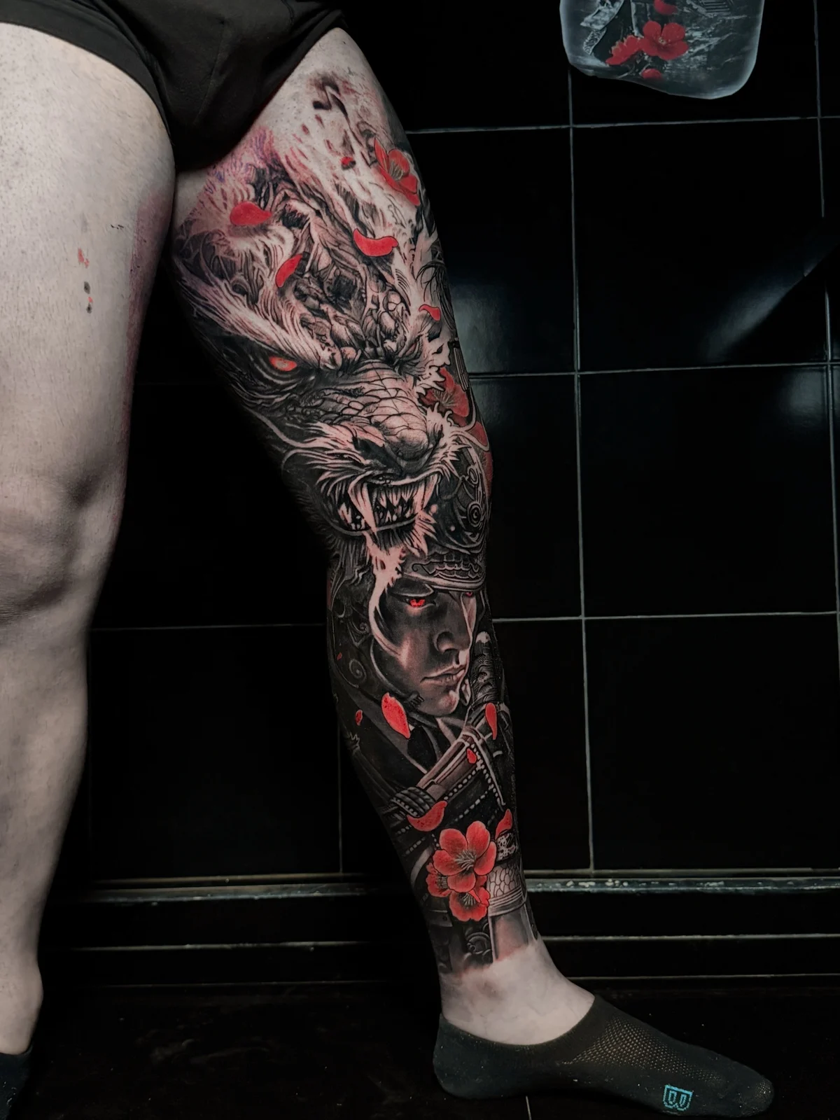 Japanese full leg sleeve with snarling dragon and samurai portrait, both with glowing red eyes and red cherry blossoms at Bloodline Tattoo Phuket.