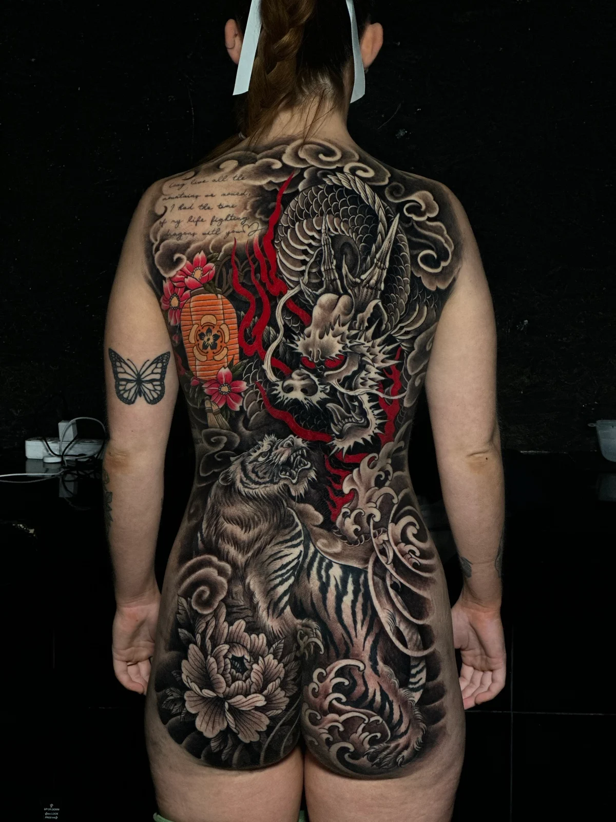 Japanese full-back irezumi with dragon, tiger, peony, paper lantern, and cherry blossoms in black and grey with red accents at Bloodline Tattoo Phuket.