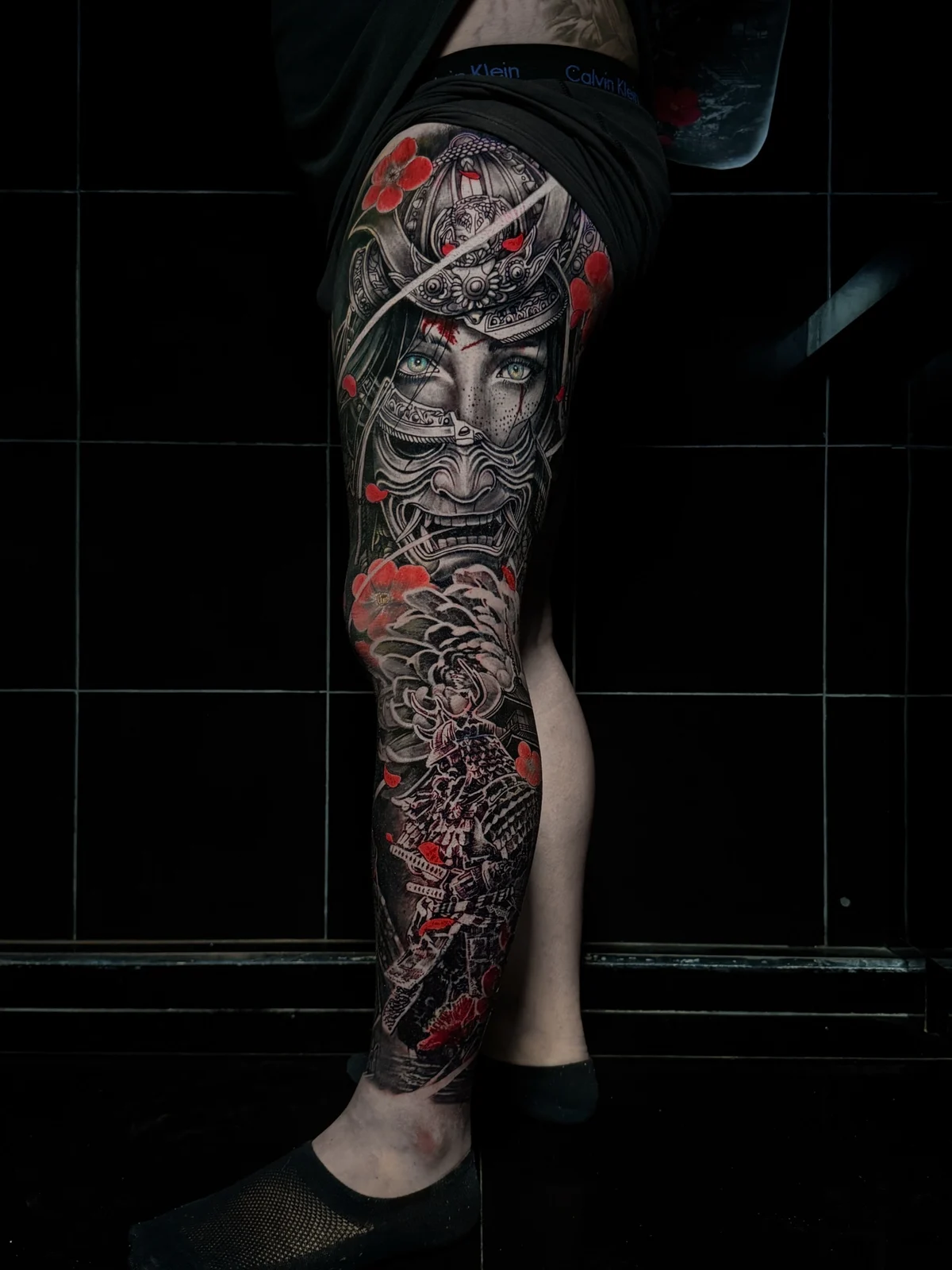Japanese full leg sleeve with female samurai in kabuto and menpo above a full-armoured warrior and red floral accents at Bloodline Tattoo Phuket.