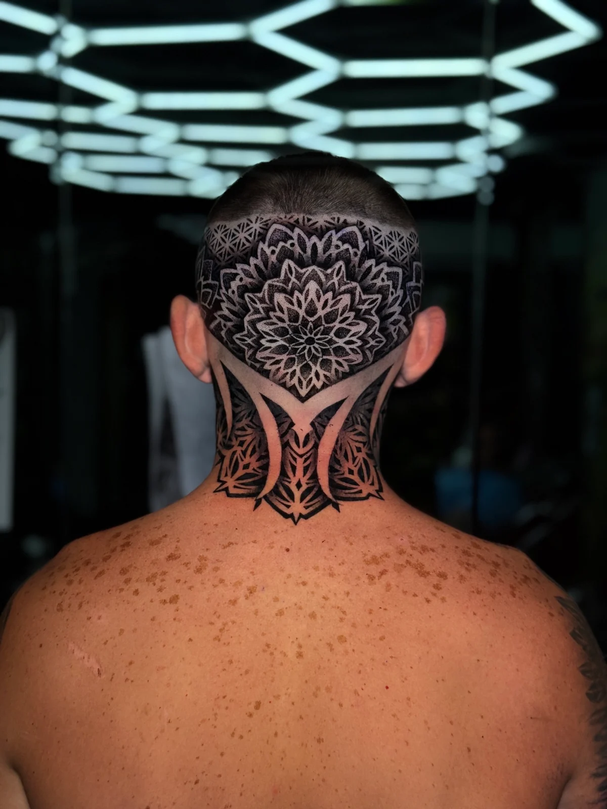 Back-of-head and neck geometric mandala with a central occipital lotus, Flower of Life crown pattern, and bold symmetrical neck panels in dotwork, at Bloodline Tattoo Phuket.