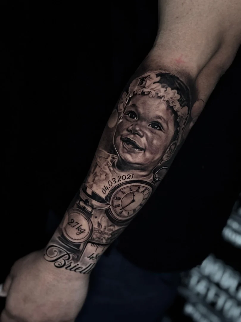 Black and grey portrait realism forearm tattoo of baby Brielle with birth date, pocket watch, weight scale, and length details at Bloodline Tattoo Phuket.
