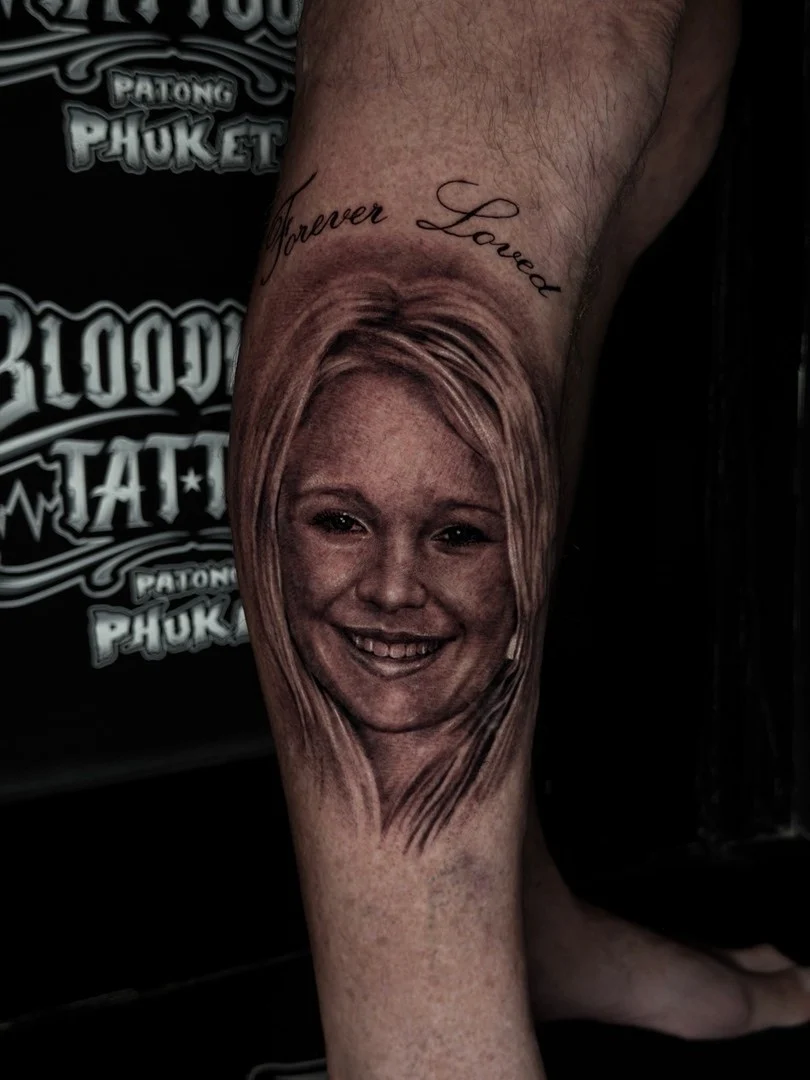 Black and grey portrait realism calf tattoo of a smiling young woman with Forever Loved script at Bloodline Tattoo Phuket.