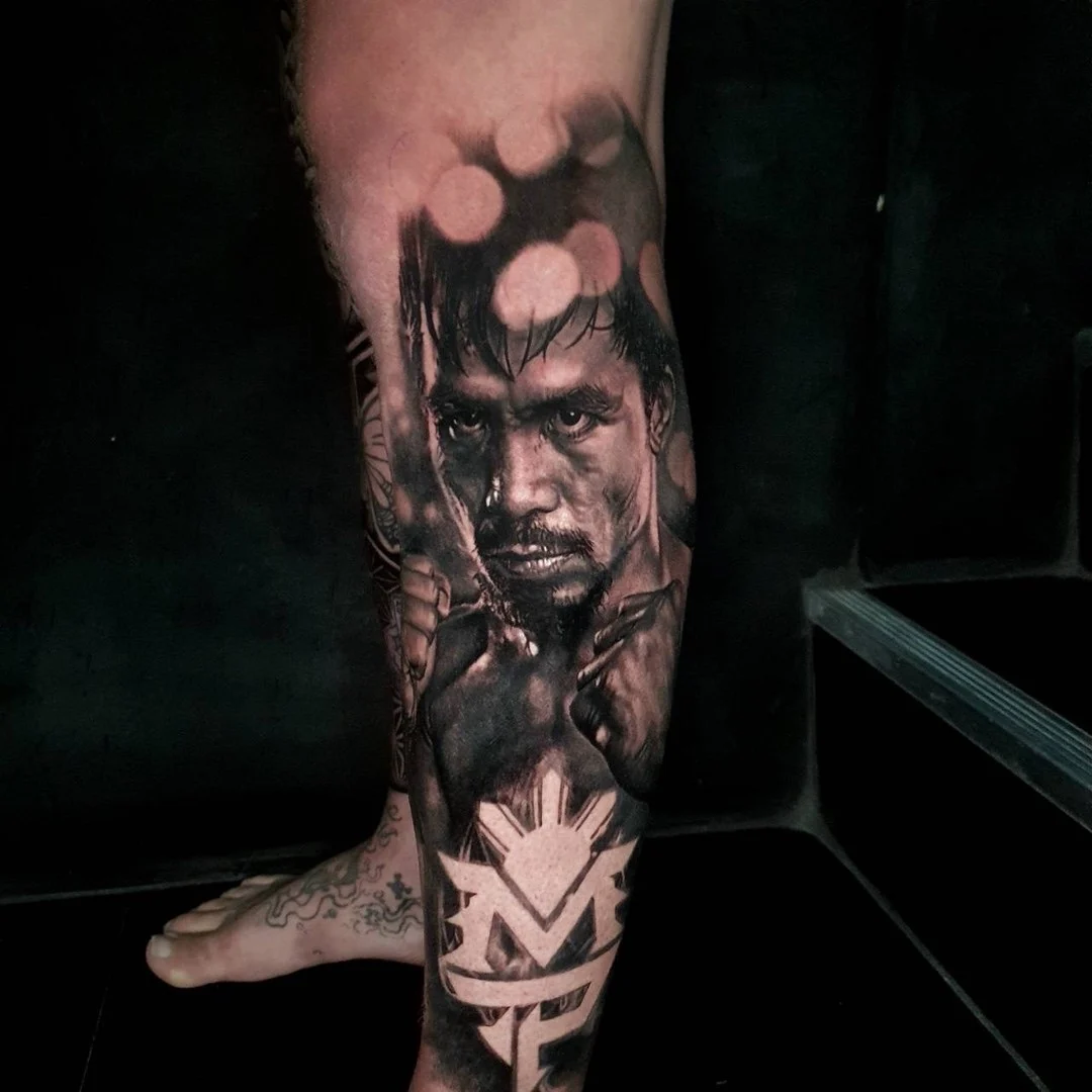 Black and grey portrait realism calf tattoo of Manny Pacquiao with MP logo and Philippine sun emblem at Bloodline Tattoo Phuket.