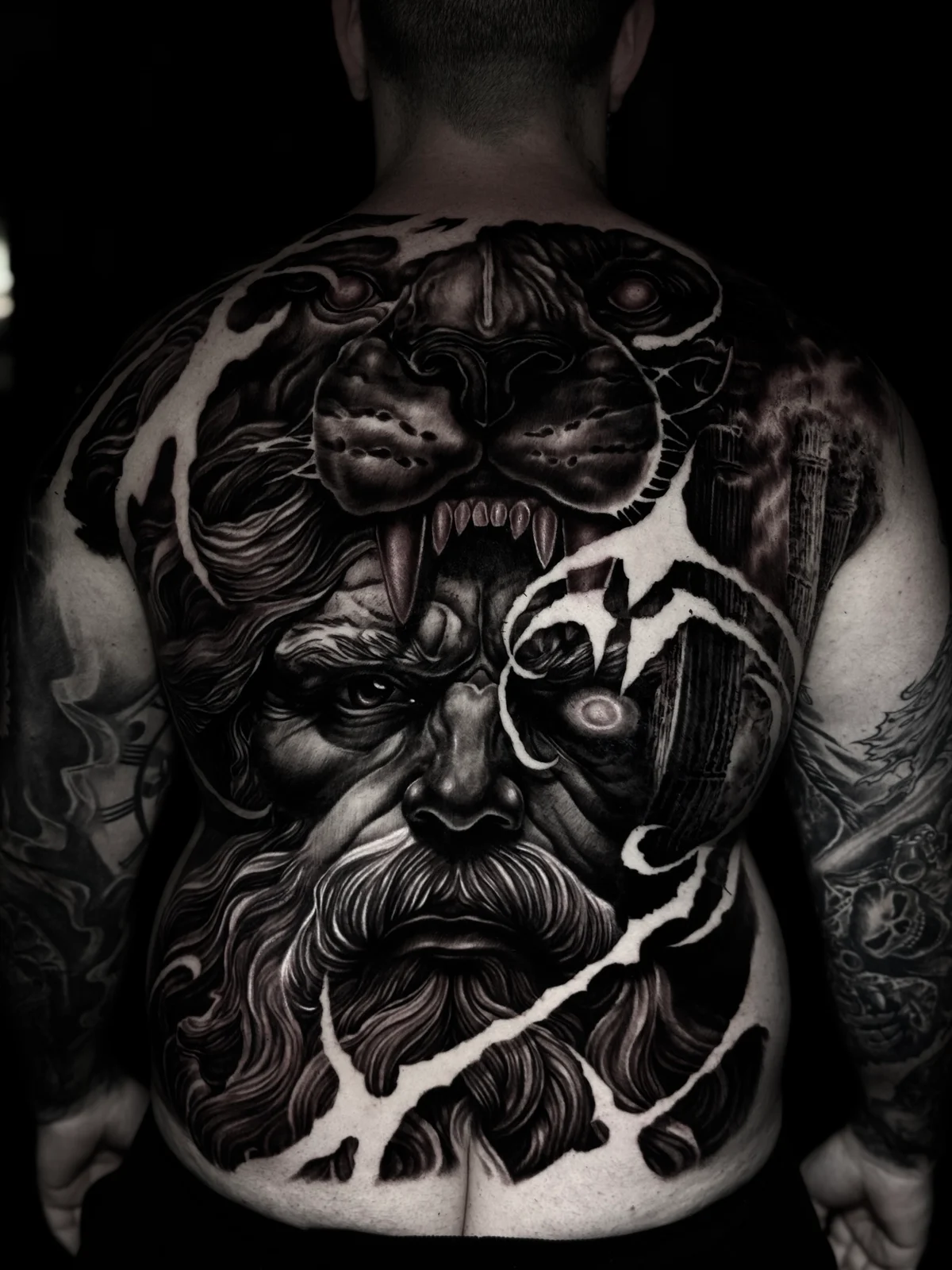 Detailed black and grey realism full back tattoo featuring Hercules in a lion-head cowl with glowing eye, classical columns, and lightning-torn composition at Bloodline Tattoo Phuket.