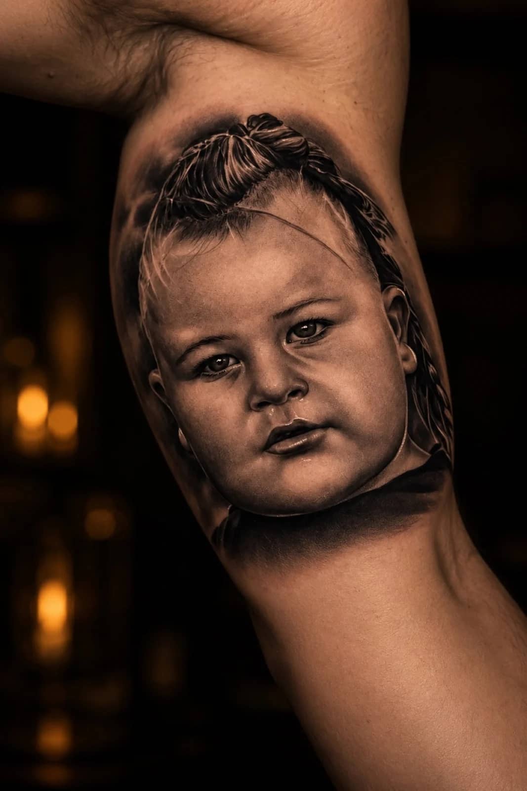 Black and grey child portrait realism with braided hair on the inner upper arm at Bloodline Tattoo Phuket